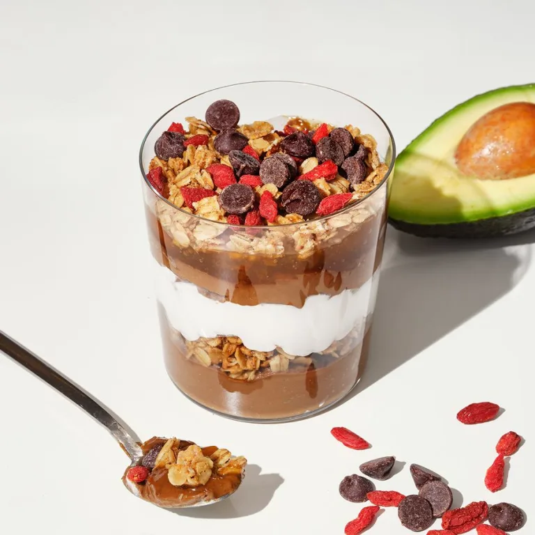 Serotonin Glow Parfait layered with chocolate mousse, yogurt, granola, berries, and cacao nibs beside sliced avocado.