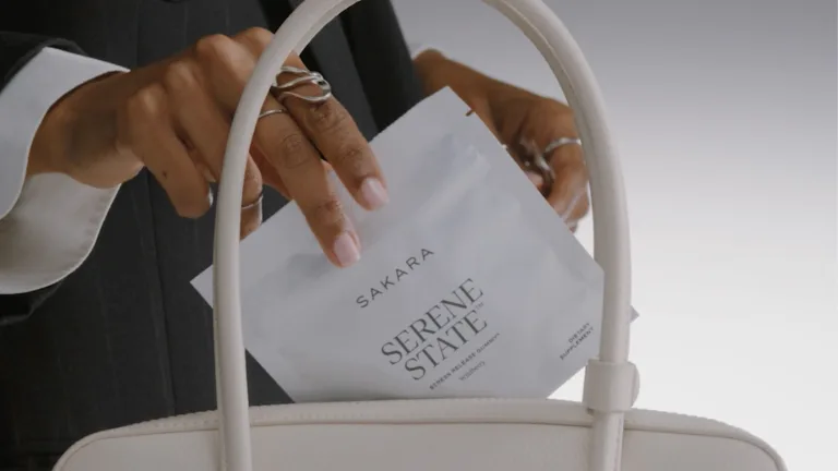 Hand placing a Sakara Serene State pouch into a white handbag.