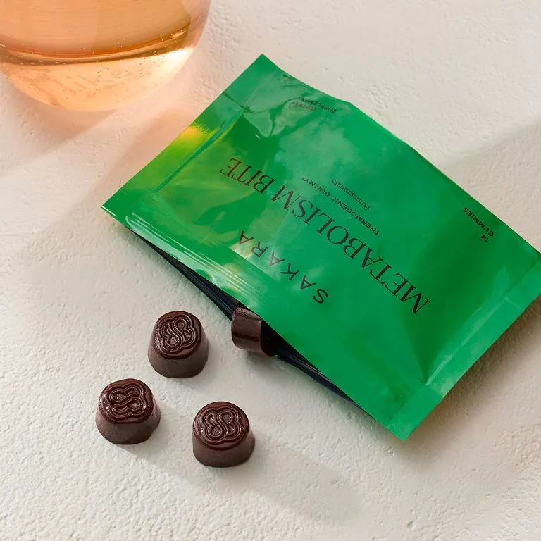Sakara Metabolism Bite in a green resealable pouch displayed with three purple gummies on a light surface.