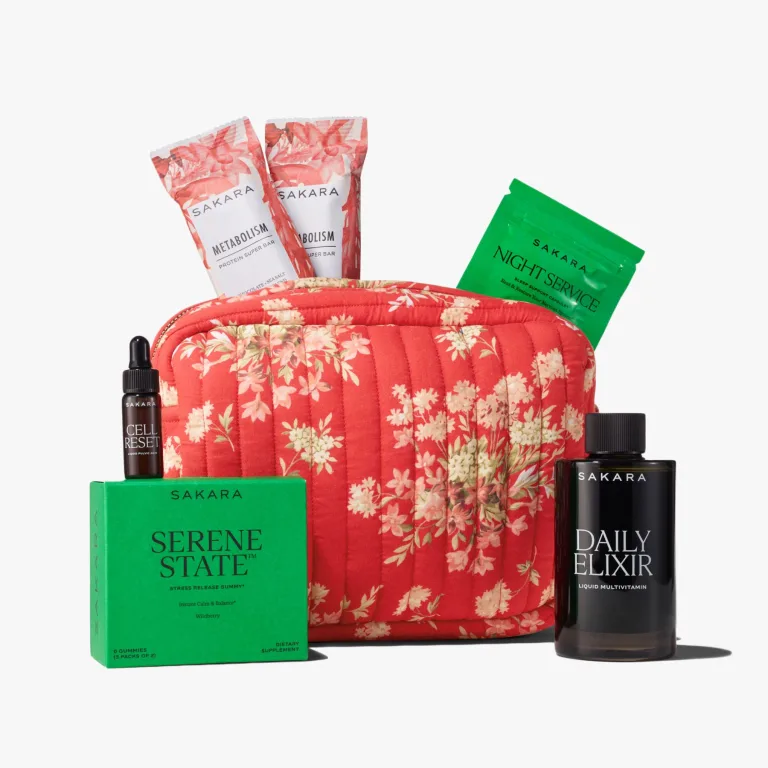 Sakara x DÔEN Holloway Pouch in red quilted floral cotton shown with Daily Elixir liquid multivitamin deluxe sample 3.25 fl oz, Cell Reset deluxe sample 0.17 fl oz, Serene State gummies 3 packs of 2, Night Service deluxe sample 6 capsules, and 2 Metabolism Protein Super Bars 45g each.