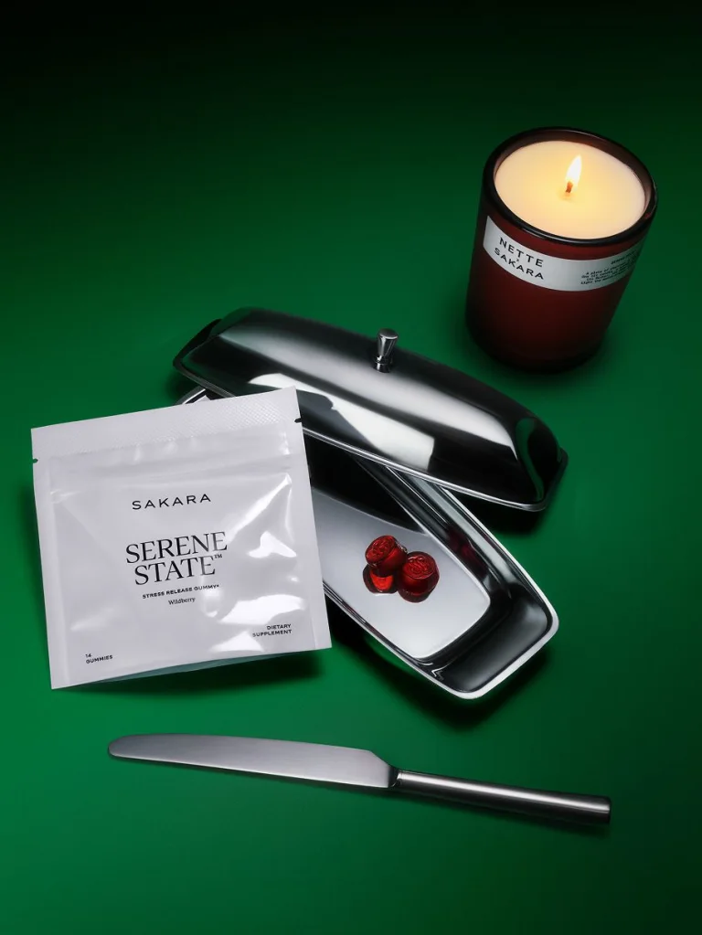Serene State stress support gummies displayed in a white pouch beside a lit Nette candle and a silver tray holding red gummies.