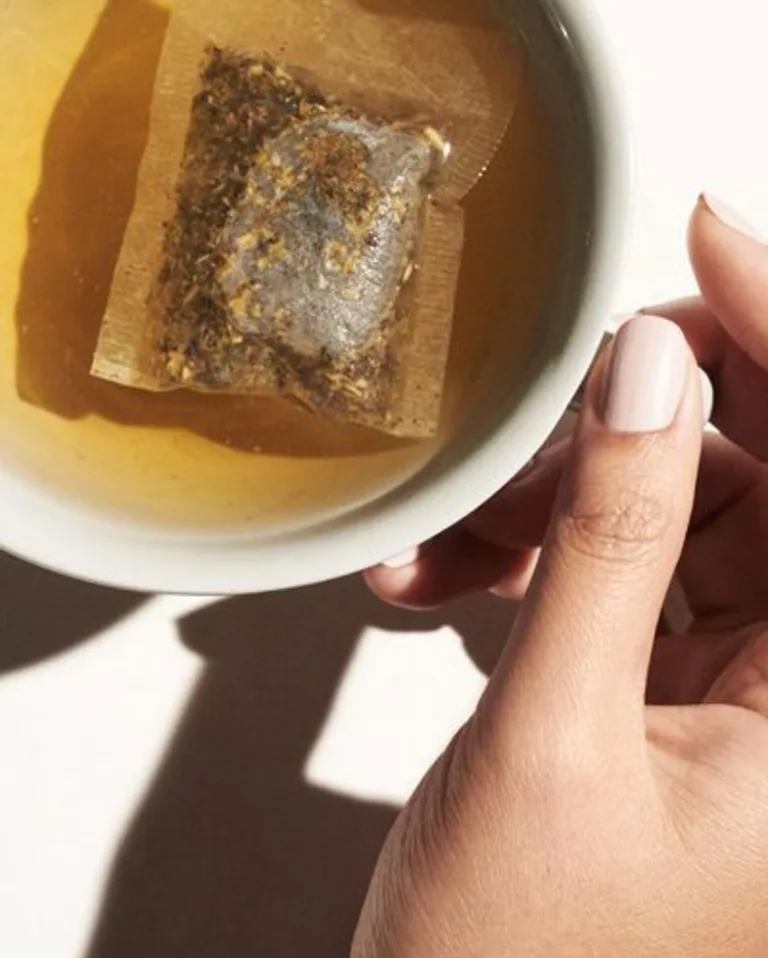 Cup of tea with a tea bag resting inside, held by a hand.