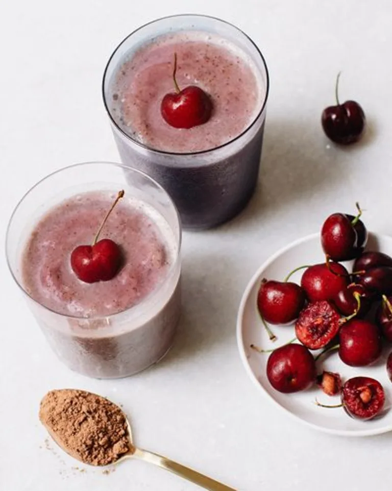 Chocolate-Cherry Metabolism Super Smoothies in glasses topped with whole cherries, with fresh cherries and Metabolism Super Powder nearby in a spoon.