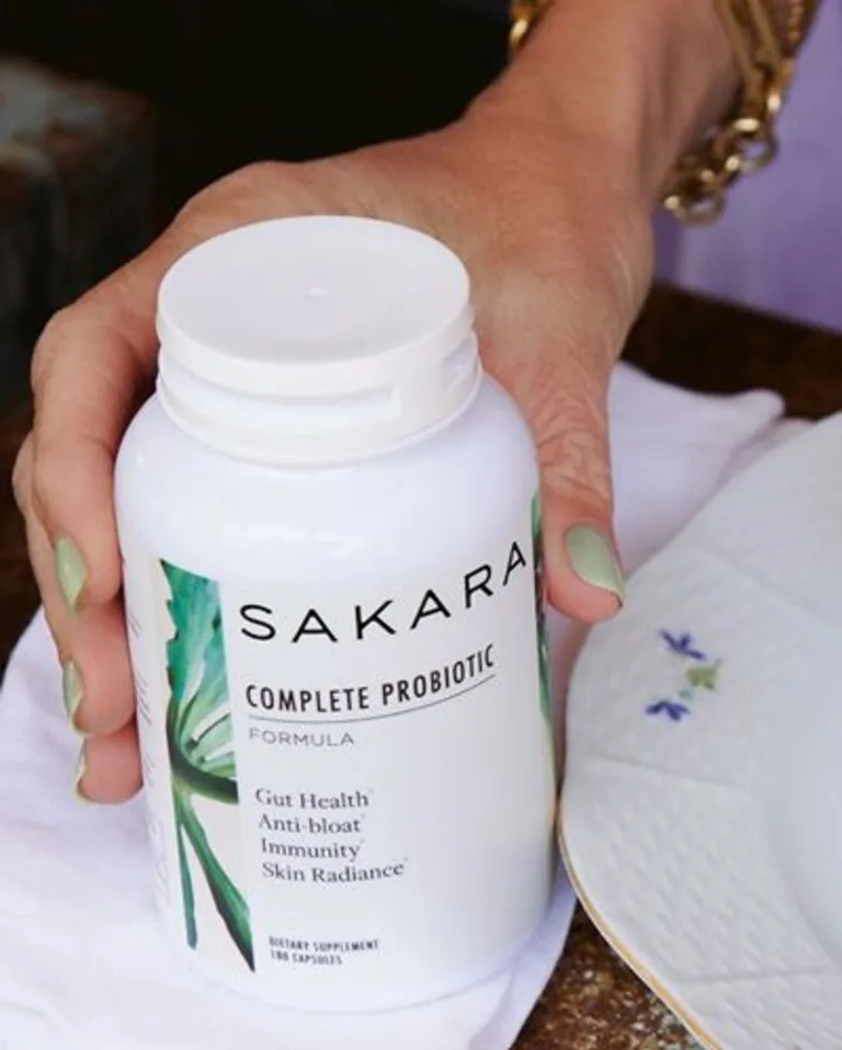 A hand holding Sakara Complete Probiotic bottle.