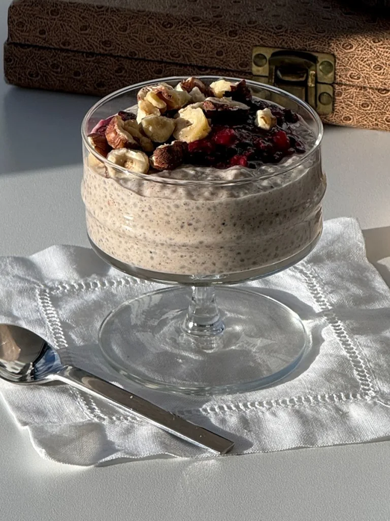 Chia pudding parfait topped with nuts and dried fruit, sitting on a white linen napkin with a spoon.