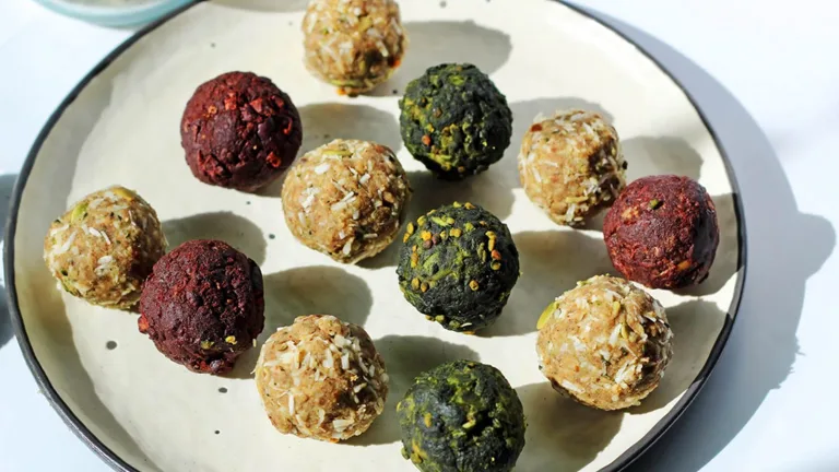 Plate of assorted energy bites in red, brown, and green colors, coated with seeds and coconut.