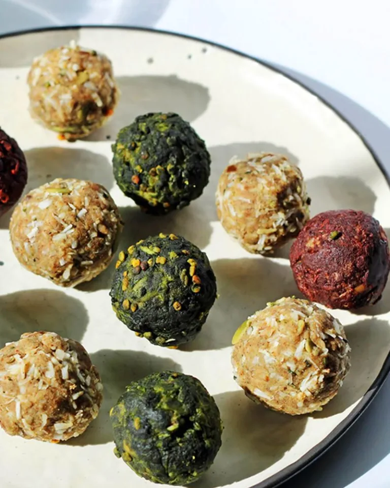 Plate of assorted energy bites in red, brown, and green colors, coated with seeds and coconut.