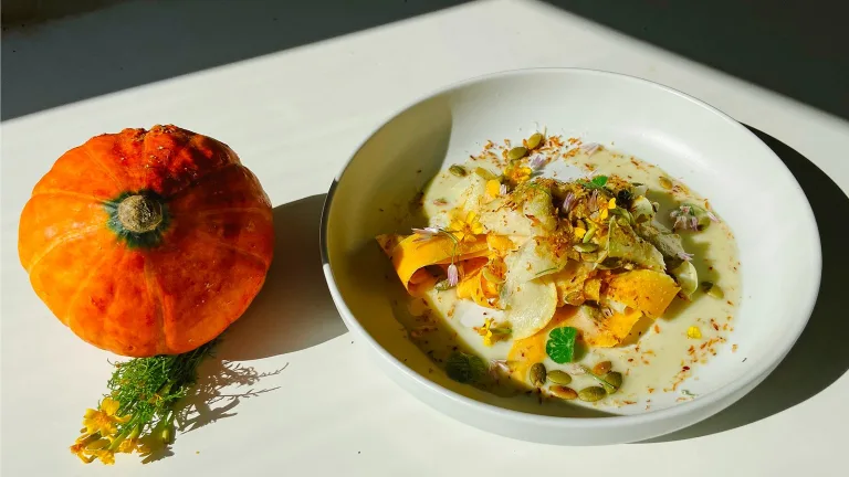 Small orange pumpkin placed beside a plated shaved butternut squash salad.