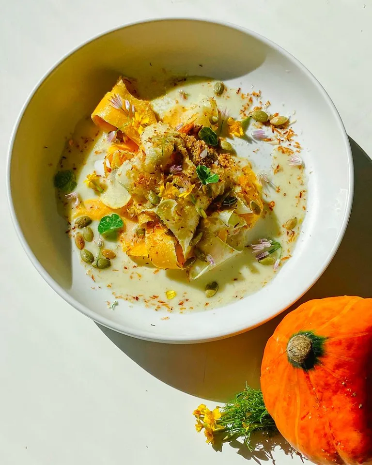 Small orange pumpkin placed beside a plated shaved butternut squash salad.