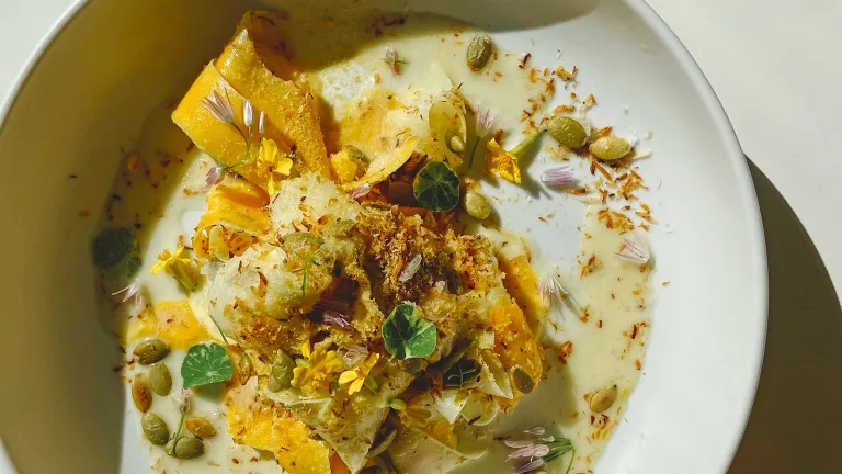 Plated shaved butternut squash salad topped with seeds and green leaves.