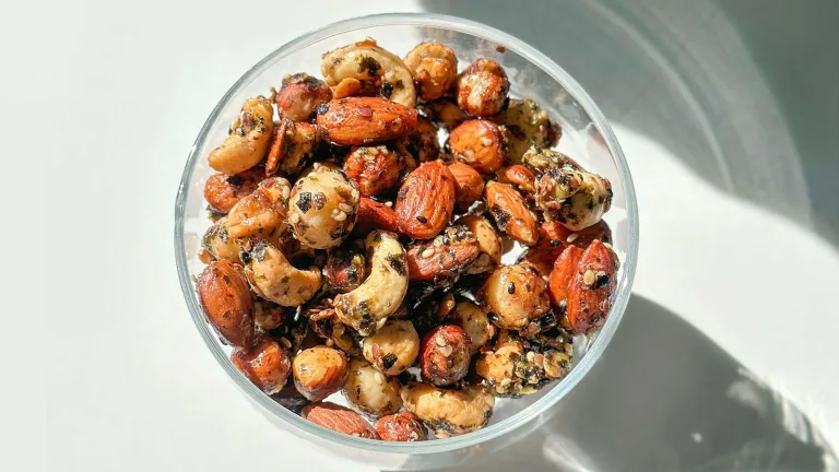 Bowl of mixed seasoned roasted nuts on a white surface.