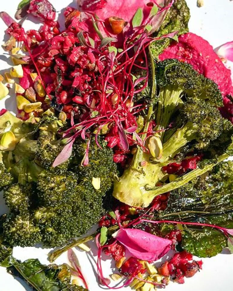 White plate with roasted broccolini and colorful shredded vegetables arranged on top.