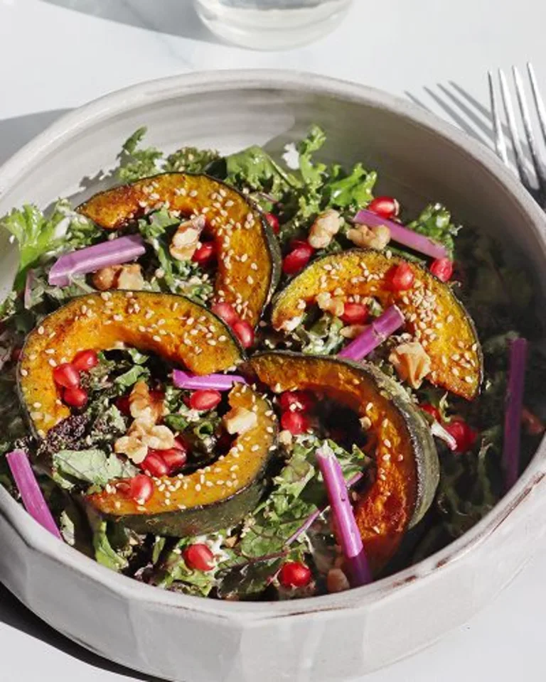 Salad topped with roasted squash slices, pomegranate seeds, and greens in a shallow bowl.