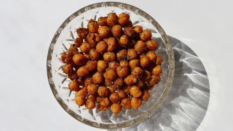Glass bowl of seasoned roasted chickpeas on a light surface.
