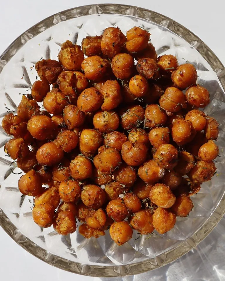 Glass bowl of seasoned roasted chickpeas on a light surface.