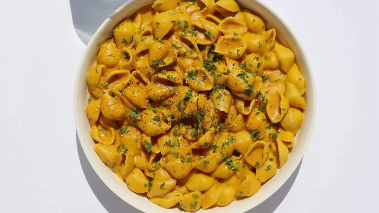 Bowl of shell pasta coated in vegan cheese sauce and garnished with herbs.