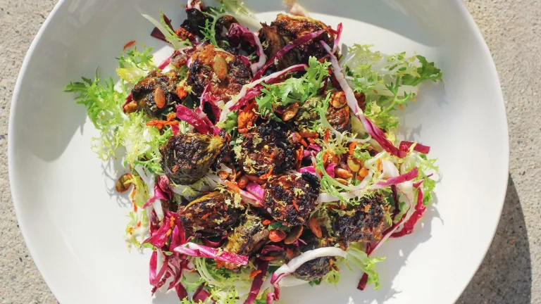 White bowl filled with a colorful salad topped with roasted vegetables, crunchy balsamic brussel sprouts and leafy greens.