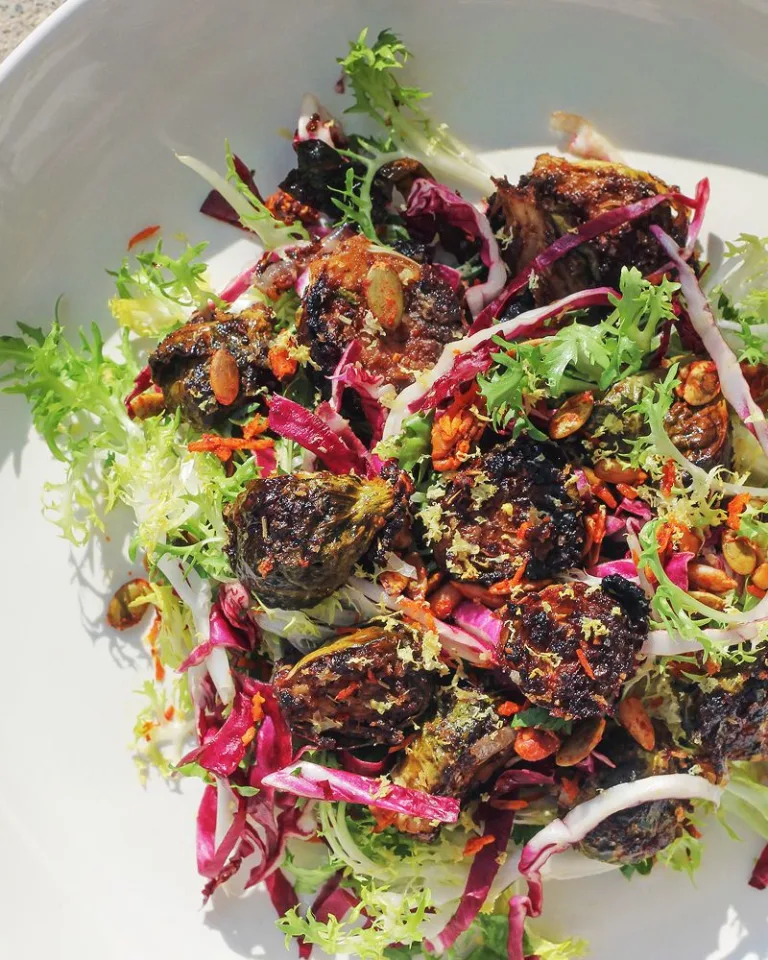 White bowl filled with a colorful salad topped with roasted vegetables, crunchy balsamic brussel sprouts and leafy greens.