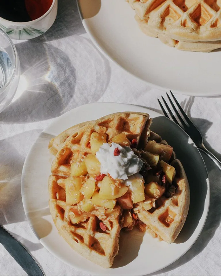 Plate of waffles topped with warm fruit compote and yogurt beside a glass of coffee.