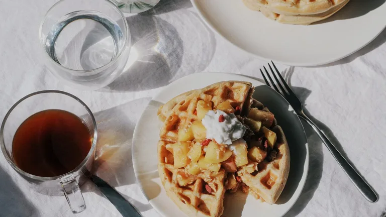 Plate of waffles topped with warm fruit compote and yogurt beside a glass of coffee.