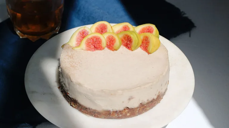 Round frosted tahini cake topped with sliced figs on a white plate.
