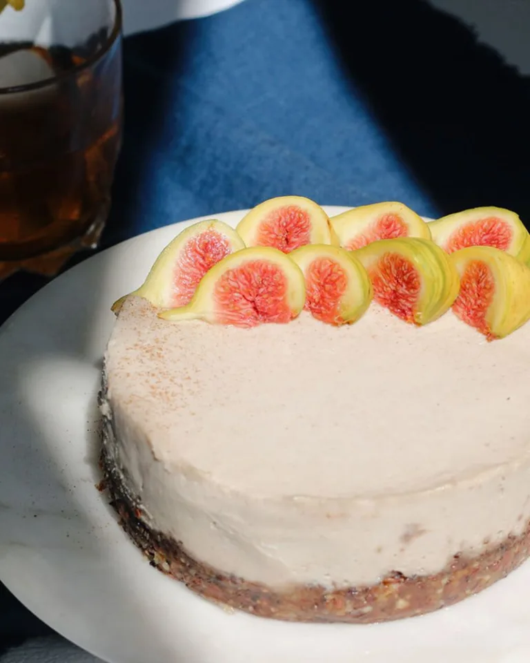 Round frosted tahini cake topped with sliced figs on a white plate.