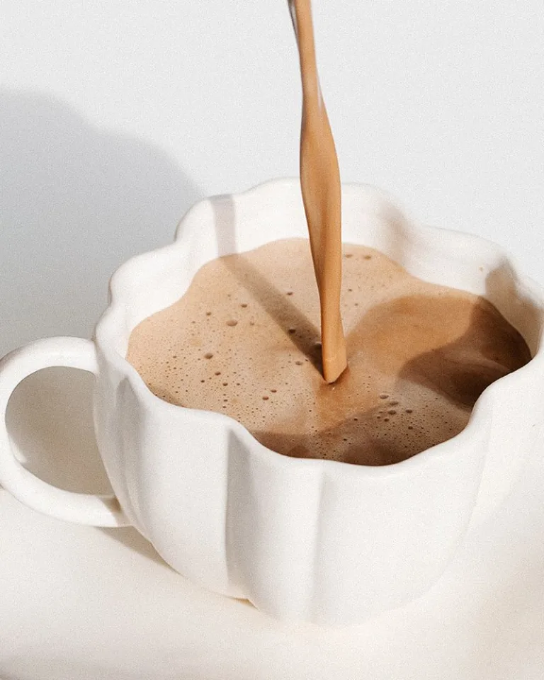 White mug filled with frothy cinnamon mocha latte, mid-pour.