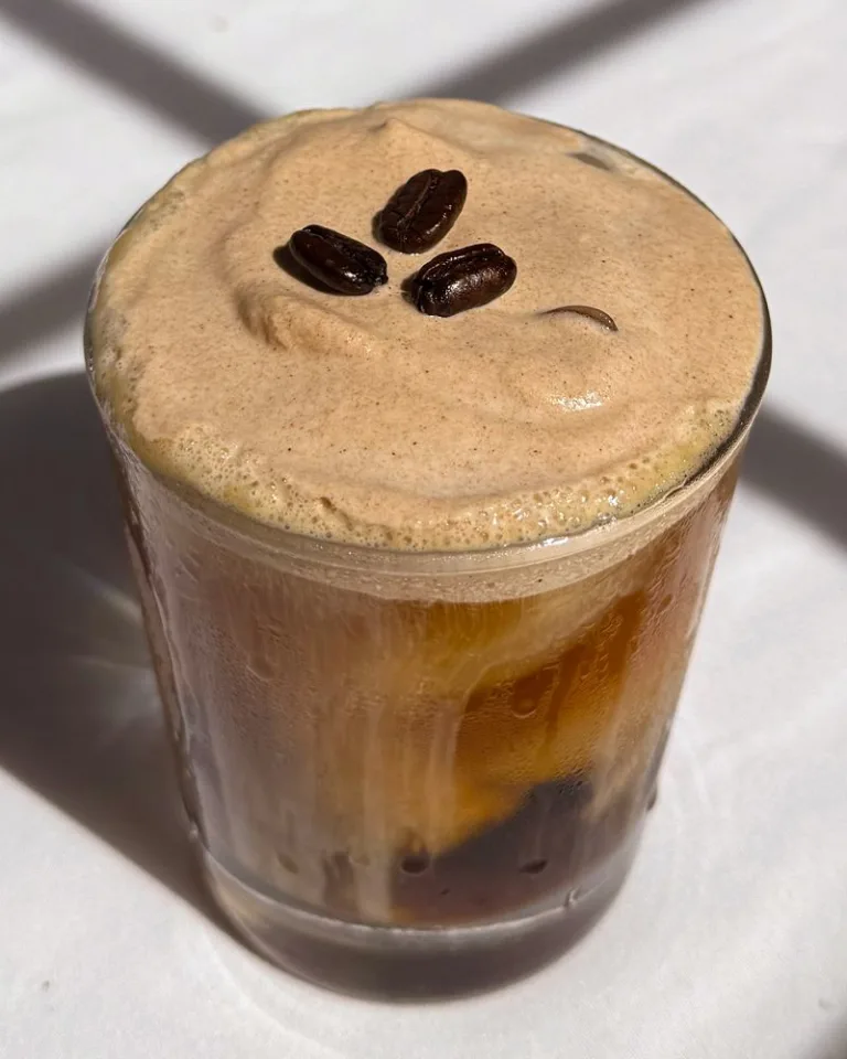 Layered iced coffee topped with foam and coffee beans.