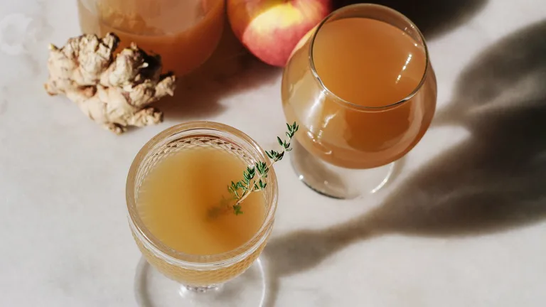 Assorted apple orchard cider in glasses arranged on a marble surface with ginger root and fruit in the background.