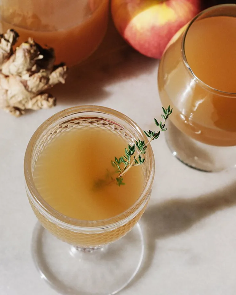 Assorted apple orchard cider in glasses arranged on a marble surface with ginger root and fruit in the background.