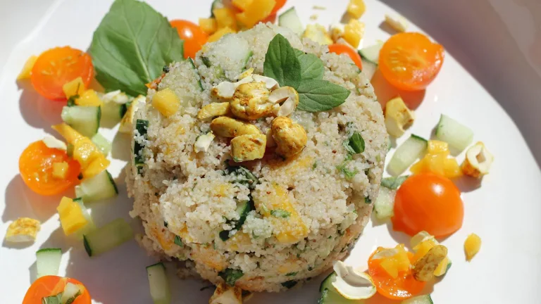 Couscous-style salad mound topped with herbs and surrounded by chopped vegetables.