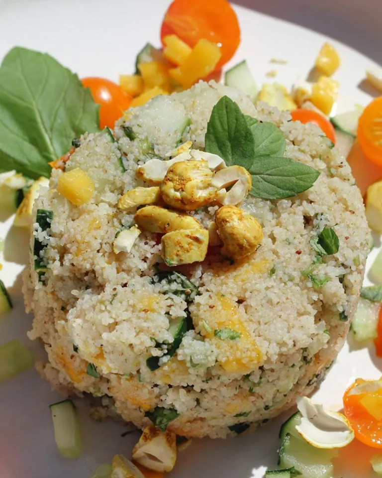 Couscous-style salad mound topped with herbs and surrounded by chopped vegetables.