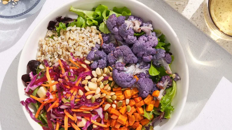 Colorful grain and vegetable bowl with purple cauliflower, carrots, cabbage, and seeds.