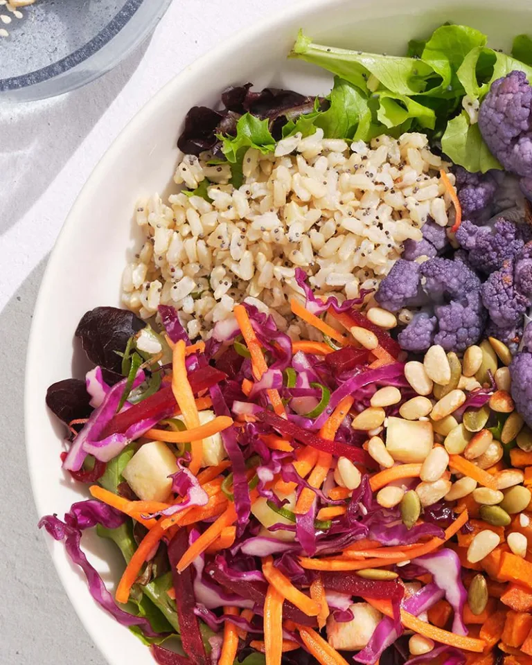 Colorful grain and vegetable bowl with purple cauliflower, carrots, cabbage, and seeds.