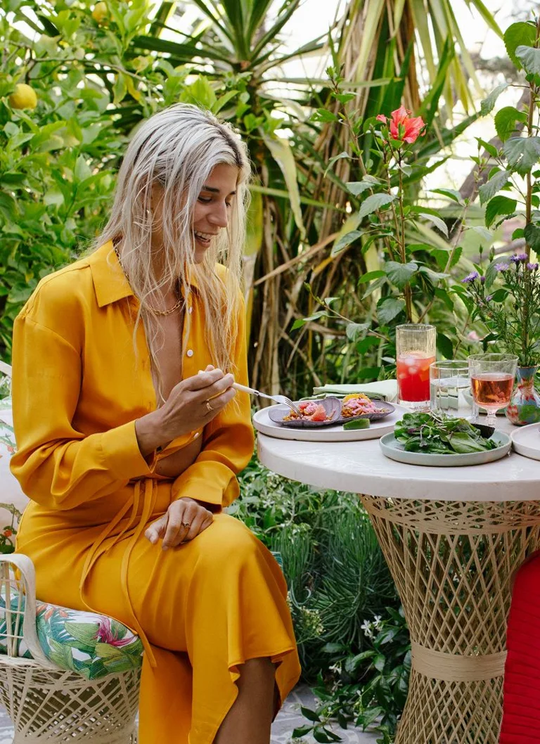 Two women sitting at an outdoor table in a garden, eating and drinking together.