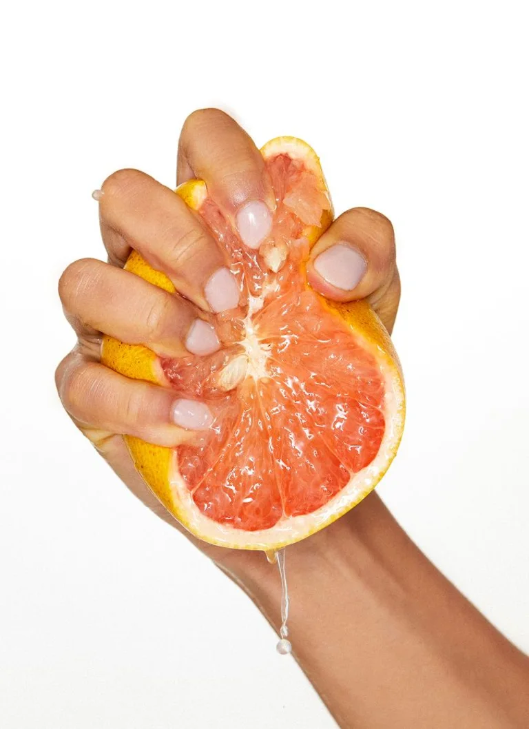 A hand squeezing half a grapefruit.