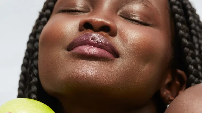 Close-up of a woman’s face with eyes closed, resting beside a green apple.