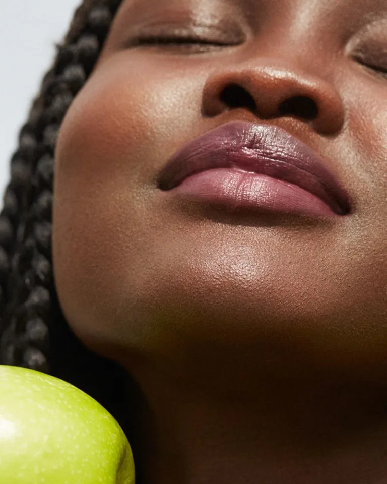 Close-up of a woman’s face with eyes closed, resting beside a green apple.