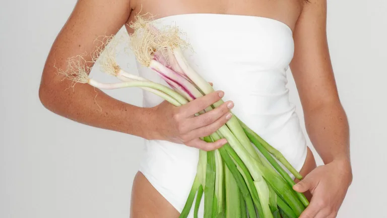 Person in a white one-piece holding a bundle of fresh scallions.