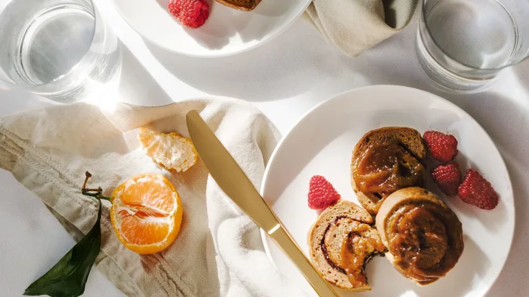 Breakfast plate with cinnamon rolls topped with caramel sauce, raspberries, peeled citrus, and a knife on a white tablecloth.