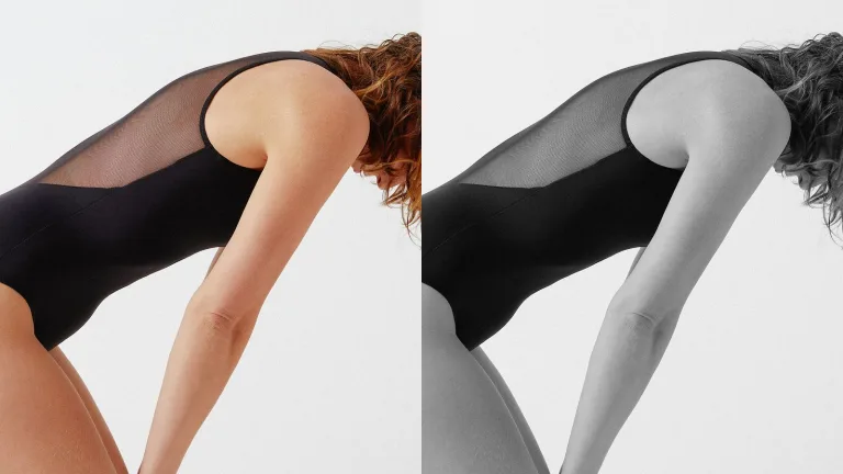 Woman in a black bodysuit leaning forward against a white background.