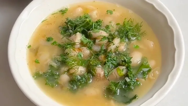 Bowl of vegetable soup topped with fresh herbs and chopped greens.