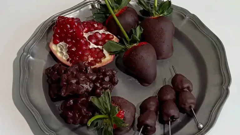 Silver platter with dark chocolate covered strawberries, raspberries, and pomegranate seeds.